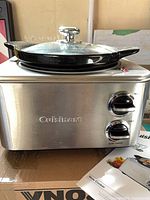 Front view of stainless steel Cuisinart slow cooker on box with manual visible