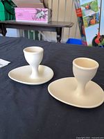 Two milky white porcelain egg cups with attached saucer sections displayed on table