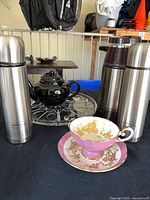 Overview of lot showing two stainless Thermos bottles, brown carafe, black teapot, glass tray and teacup set