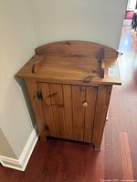 Front view of small wooden cabinet showing door, knob, hinges, decorative backsplash and finish