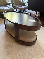 Angled view showing oval dark wood coffee table, top surface, lower shelf with beige cushion