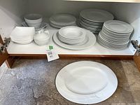 Cabinet shelf showing stacks of dinner plates, side plates, bowls, lidded sugar bowl and large oval serving platter