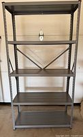Full view of gray metal shelving unit showing five shelves and cross brace