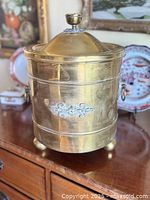 Front view of brass ash bucket showing scroll applique and ball feet