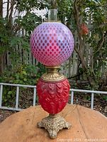 Full view of lamp showing ruby molded base, brass section, coin-dot globe, clear chimney