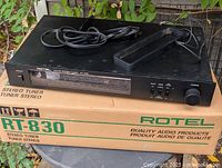 Rotel RT-830 tuner on top of original box with power cord, RCA cable, and AM loop antenna visible