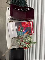 Burgundy metal gift bag, box of lights, holly sprays visible
