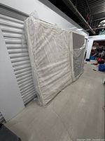 Mattress and box spring leaning against wall, wrapped in plastic