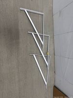 Three white metal shelf brackets laid flat