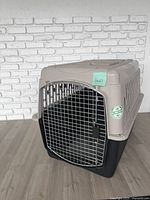 Front view of beige and black plastic kennel with metal wire door closed