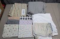 All folded linens displayed on surface showing duvet cover, two white sheets and eight assorted pillowcases