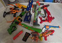 Group shot of all blasters, bow, drum, clip and darts laid on floor