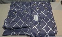 Four folded blue curtains with silver lattice pattern and grommets visible