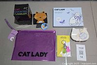 All five cat-themed items laid out: tumbler box, note set box, keychain, pouch, can sleeve