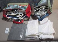 Overview of lot showing two bags filled with white plastic hangers, folded grey storage box and stacked white garment covers