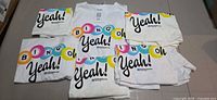 Multiple white Norwegian Cruise Line Bingo “Yeah!” T-shirts laid out showing front graphics