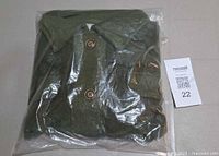 Front view of olive green jacket folded in sealed plastic bag with button placket and collar visible