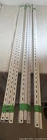 Four of the slotted white steel uprights laid out to show length and slot pattern