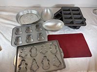 All pans and mat laid out: pumpkin pan, two egg halves, two stacked mini loaf pans, snowman pan, gingerbread/tree pan, silicone mat