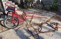Side view of red dog cart with attached wheels and harness parts on ground