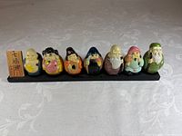 Front view of seven glazed figurines on black base with wood plaque