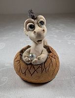 Front view of baby dragon figurine in egg holding crystal
