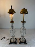 Two clear cut glass table lamps, one illuminated, on square brass bases