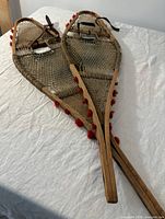 Pair of wooden snowshoes laid flat showing overall design and red pom-poms