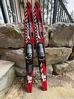 Full view of both Mercury Racing water skis leaning against rock wall