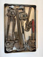 Seven vintage pipe wrenches in tray