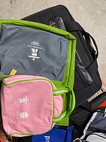 Pile of various bags showing gray and pink Vancouver 2010 totes, black laptop bag, black textured shoulder tote