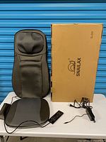 Massager cushion, box, remote, power adapter on table