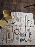 Full lot overview on fabric including necklaces, rings, bracelets, pendants, stones, and box