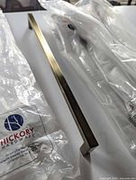 Unwrapped brushed gold bar pull beside branded Hickory Hardware packaging