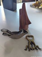 Group shot showing all three items: bird juicer, brass bottle opener, teak eyeglasses nose stand