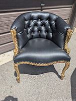 Front view of black tufted faux leather tub chair with gold rope and tassel arms and legs