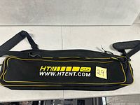 Top view of HT Enterprises black and yellow fishing bag showing logo, zipper, and shoulder strap