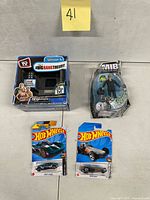 All four packaged toys laid out: Tiny TV box, MIB figure, two Hot Wheels cars