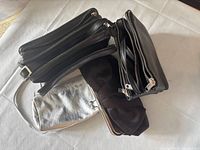 Four handbags grouped: two black multi-zip purses, one black wristlet, one silver metallic wristlet