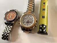 Two wristwatches beside measuring tape showing size reference