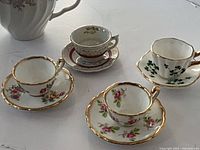 All four miniature teacup and saucer sets displayed; large regular-size cup in background not included