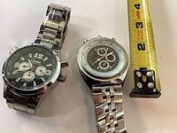 Both wristwatches side by side with tape measure for scale