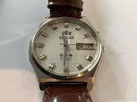 Front view of Orient automatic watch showing dial, logo, day-date window, and leather strap