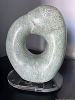 Front view of green stone serpent sculpture on lucite base showing overall form and plaque
