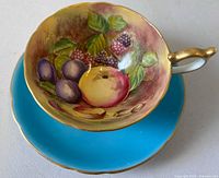 Cup resting in saucer showing turquoise saucer and interior fruit painting