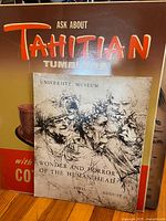 Both posters leaning against wall; Tahitian Tumblers graphic partly visible, University Museum poster in front