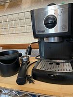 Front view of DeLonghi espresso machine with portafilter, steam wand, drip tray, knockbox