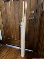 Full view of cardboard tube holding long wooden dowels