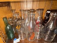 Group of assorted clear milk bottles, green soda bottle and amber beer bottle on shelf