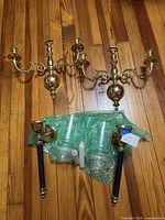 Four sconces laid out on wood floor: two three-arm brass units, two single-arm brass/black units with glass shades and candles
